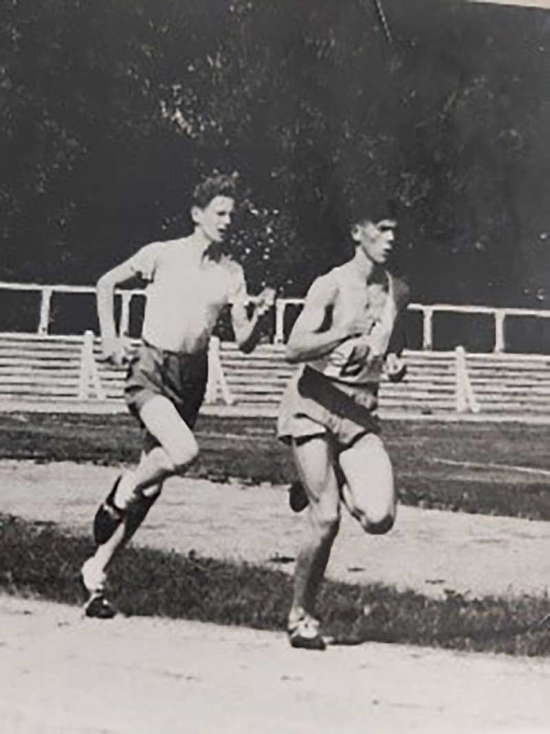 An archival image of two men running on an oval track.