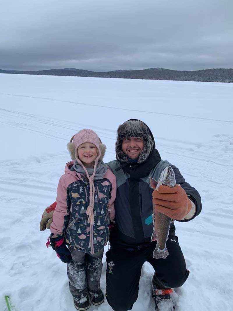 Small girl and young man on a frozen lake, the man holds a big fish.