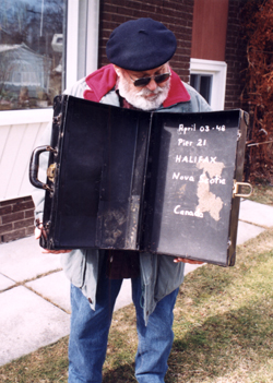 Bearded man wearing blue beret, displaying inside old, worn out suitcase.