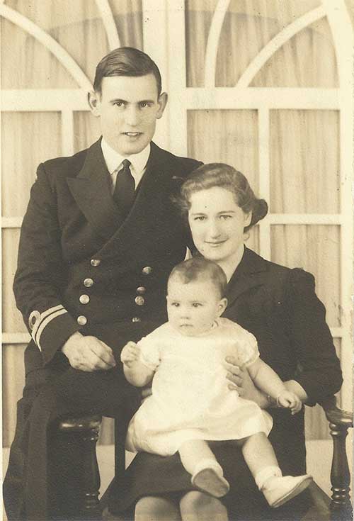 A young woman is sitting on a chair with a baby in her lap and a young man sitting on the arm chair.