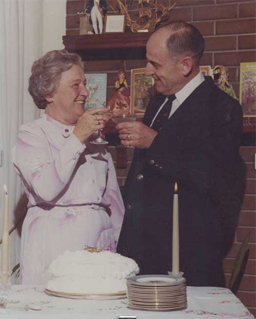 A young couple are holding glasses in their hands and there is a cake with candles on the table in front of them.