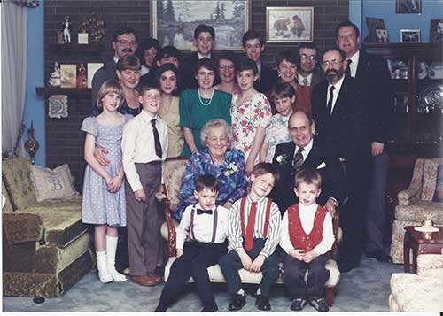 Three generations of family members are sitting and standing for a photo.