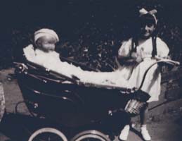 Little girl with bow in hair pushing baby doll in pram.