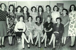 Group photograph of five young women seated and several others standing behind them.