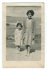 Two young girls standing at water's edge, with waves lapping in background.