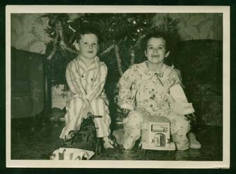 Sandra and brother Ken as children, in pyjamas, sitting in front of Christmas tree.