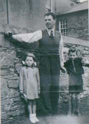 Man leaning against a stone wall, a little boy and a girl on each side.