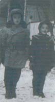 Boy and girl in winter clothes, standing in the snow.