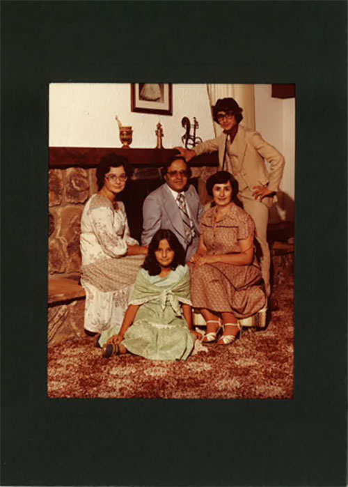 A family are sitting in front of their fireplace wearing formal clothing.