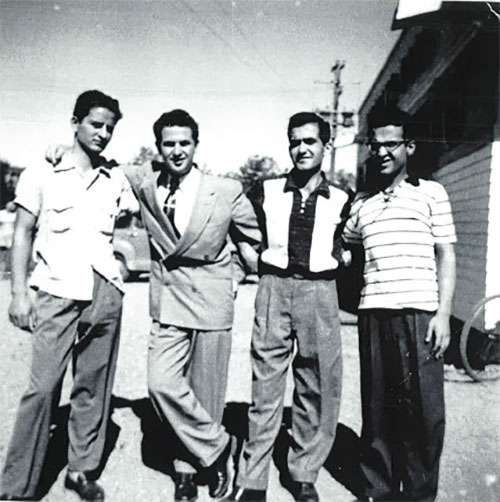 Four young men stand side by side with their arms wrapped around each other.