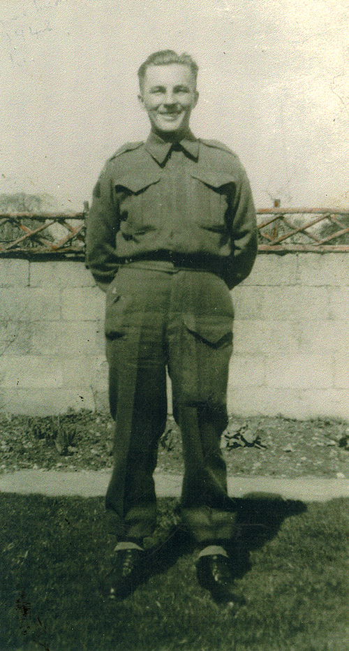 Handsome man wearing military uniform standing in front of wall with smiling face.