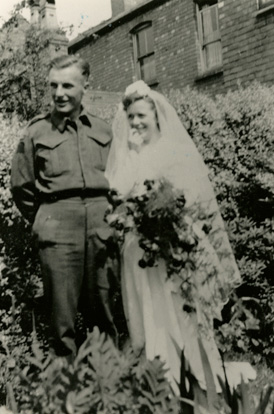 Beautiful young lady wearing wedding dress holding flowers standing with handsome man wearing army dress.
