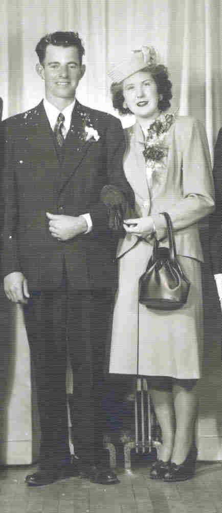 A well-dressed couple are standing in front of a backdrop for photos.