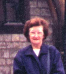 More recent photograph of older Joyce, wearing glasses and a blue coat.