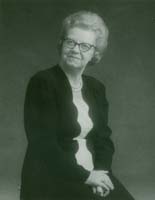 Portrait of the young Felicita, hands clasped on her knees and wearing glasses.