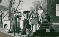 Mother, father and children sitting on, and standing by, old family truck.