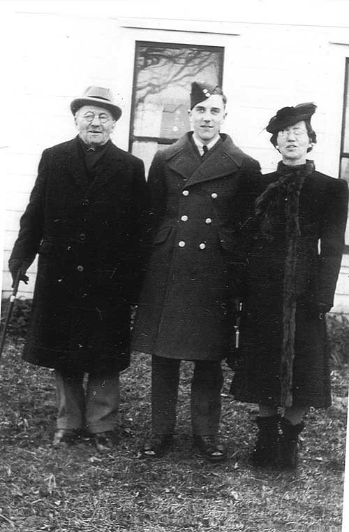 A man and woman stand on either side of a young man in a military uniform.
