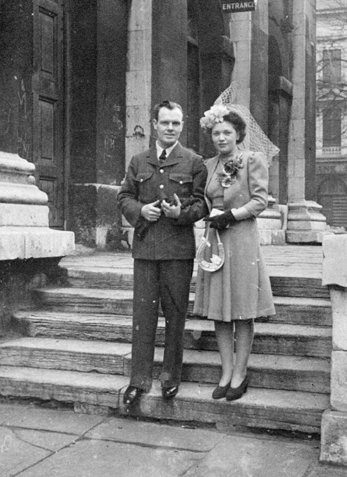 A man and woman stand on the steps of a church in wedding clothes.