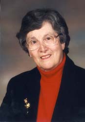 Portrait of older Catherine, wearing red turtle neck and black blazer.