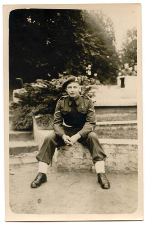 Young Hugh in military clothes, seated on stone wall.