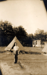 Faded photo of young William standing on a field with tents in background.