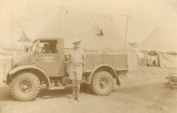 Young man in military uniform standing in front of transport truck.