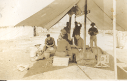 Faded photo showing several young men under a tent on military grounds.