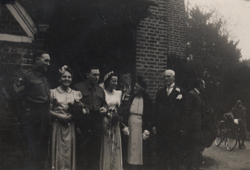 Bride, groom and bridal party standing outside brick building.