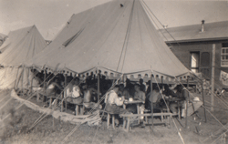 Several men eating at picnic tables under huge military canopy.