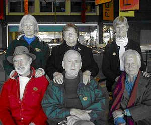 Three older men sitting at the Pier 21 Museum, their wives behind them.