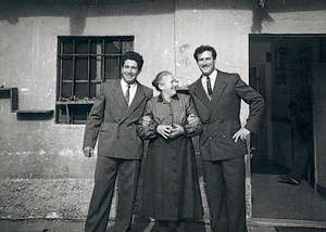 Older woman standing between two young men, in front of building.