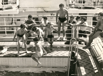 Several young boys jumping into the pool of the ship.