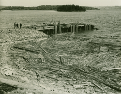 Aerial view of three men near a dock by the water, debris in the water. 