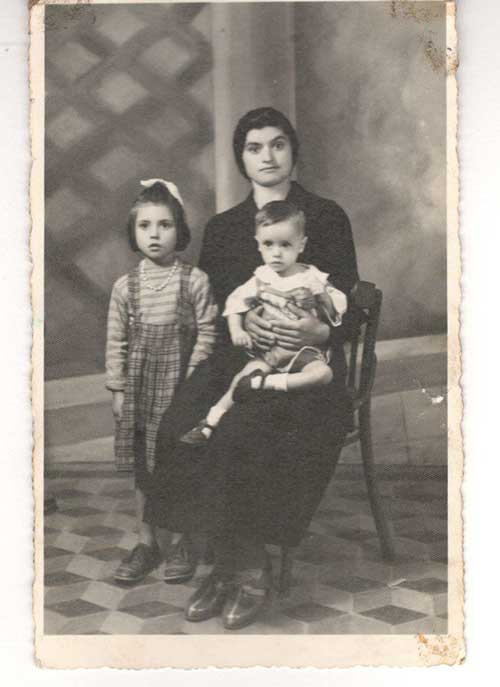 Archival photograph of a woman seated in a chair with a toddler in her lap and a young girl standing next to her.
