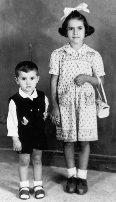 Young Luigi and sister, sister has big ribbon in hair and holds a white purse.