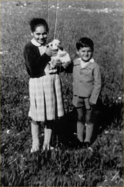 Luigi and sister as children, standing in a field with a small dog.