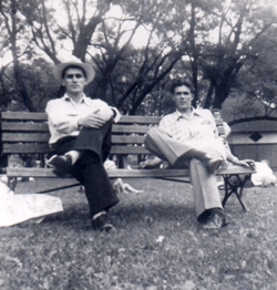 Two young men seated on a park bench in summer.