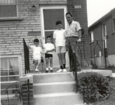 Giovanni and three small children on cement steps in front of house.