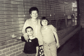 Maria with two small grandchildren in front of Wall of Honour at Pier 21.