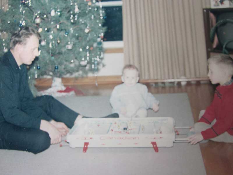 A man and small child sit in front of a Christmas tree, looking at toys.