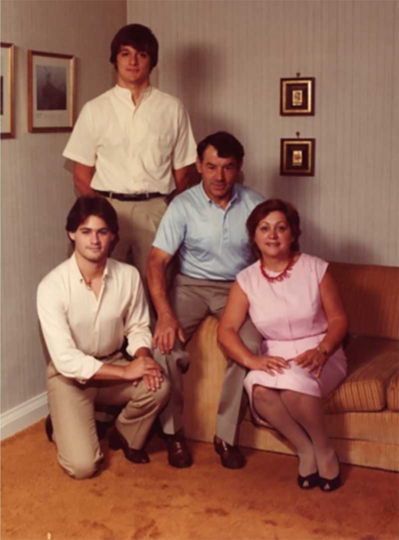 A family pose inside their living room; mother and father are on the couch and their two sons are next to them.