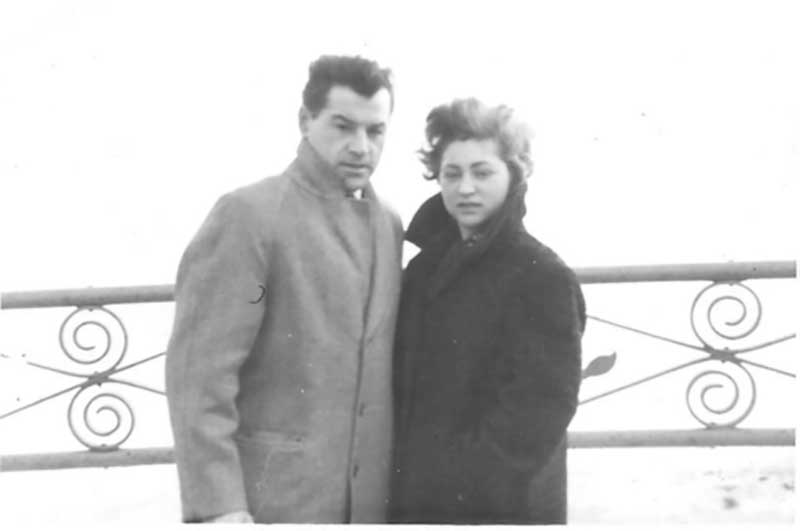 A man and woman are dressed in winter coats as they stand on the deck of a ship.