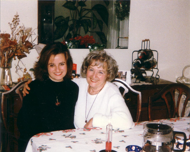 Two women seated at the dinner table link arms and smile for the camera.