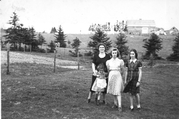Three young women with small girl, standing in an open field.