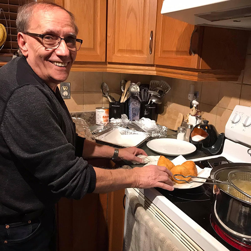 A smiling man is cooking something on the stove.