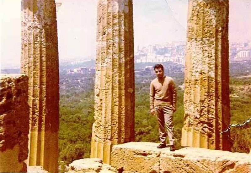 A man stands between two columns on an ancient ruins site.