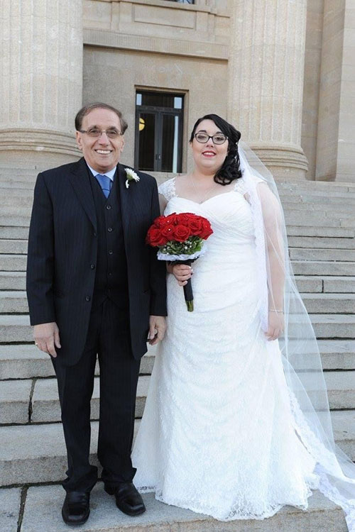 A man stands next to his daughter in front of a church, it is her wedding day.