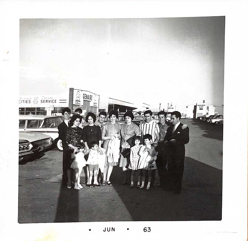 A group of men, women and children stand together in a parking lot.