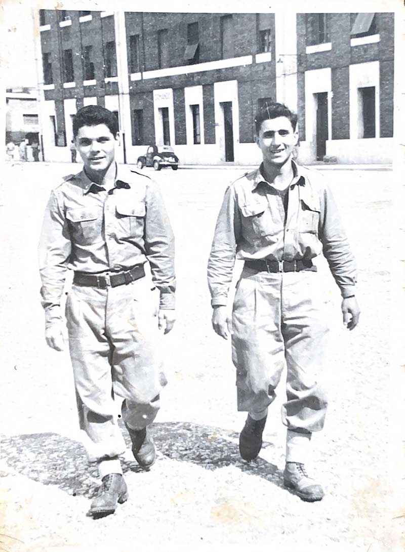 Two men in similar military uniforms walk toward the camera.