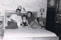 Man and woman seated on bed with small child between them.